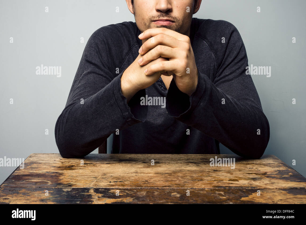 Giovane uomo seduto a tavola con le sue mani piegate Foto Stock