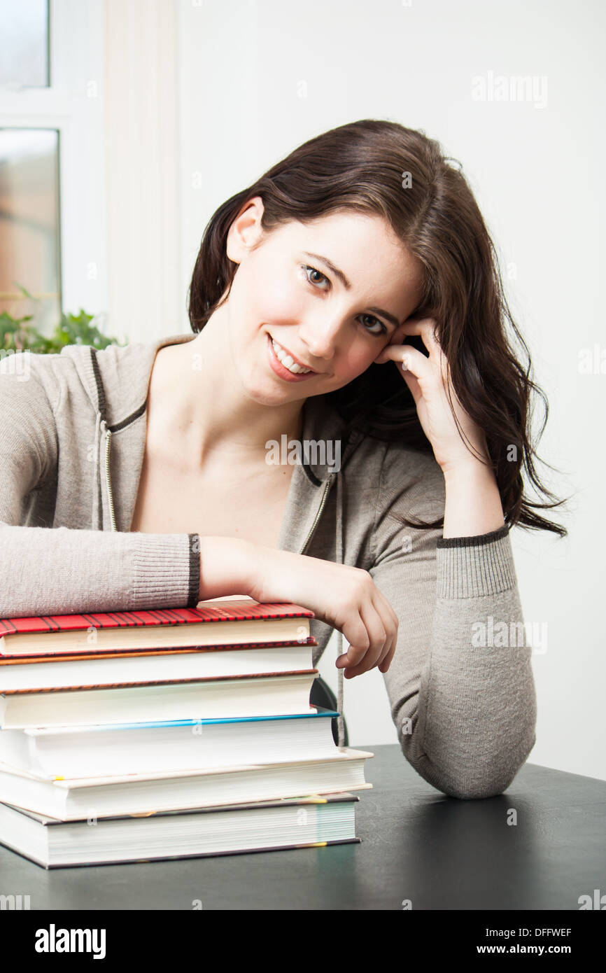 Bella bruna college ragazza sorride alla telecamera mentre appoggiato su una pila di libri di testo. Composizione verticale Foto Stock