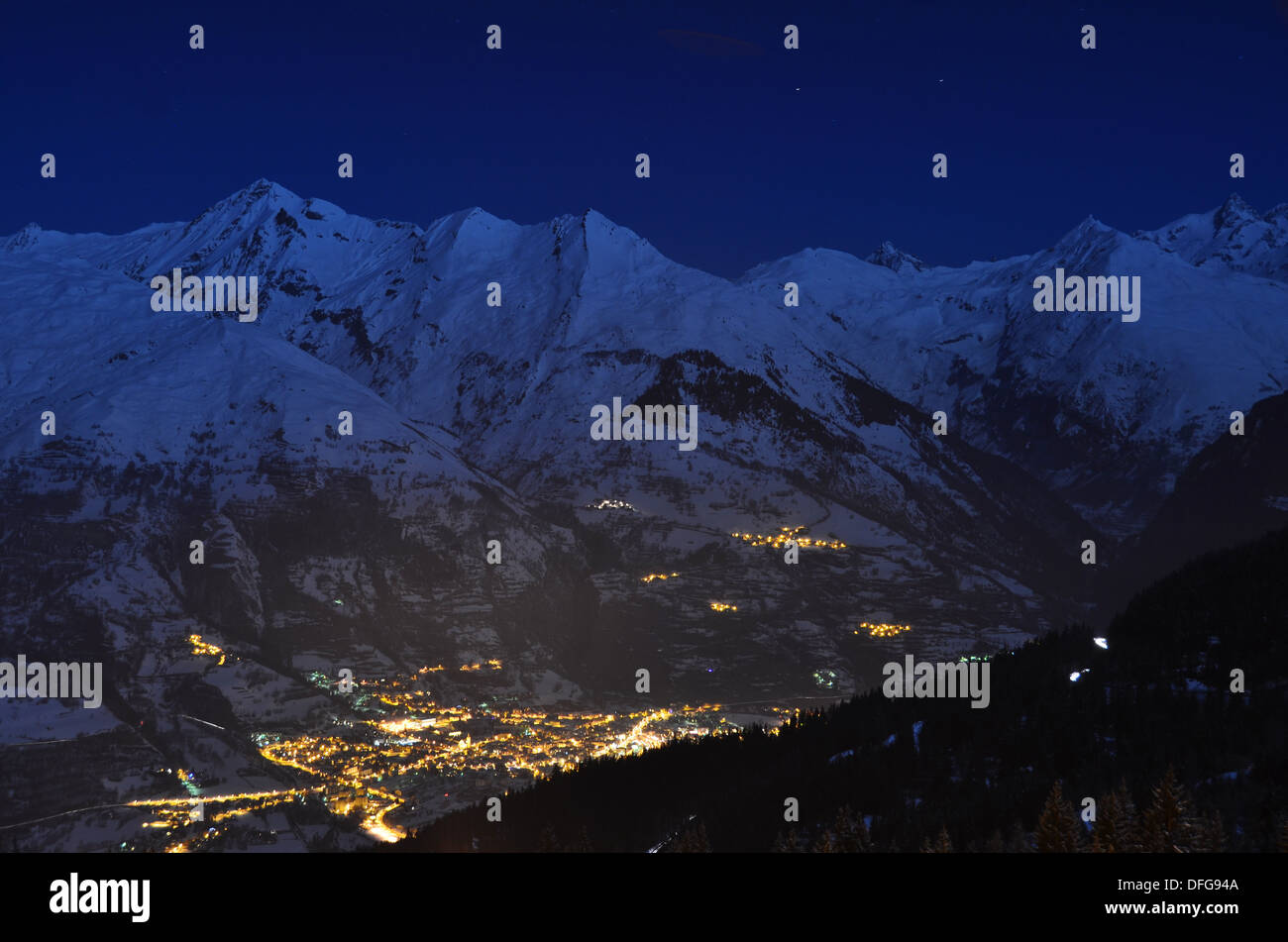 Alpi francesi della Tarentaise valley sono illuminati dalla luna come i lampioni di Bourg Saint Maurice candelette di seguito. Foto Stock