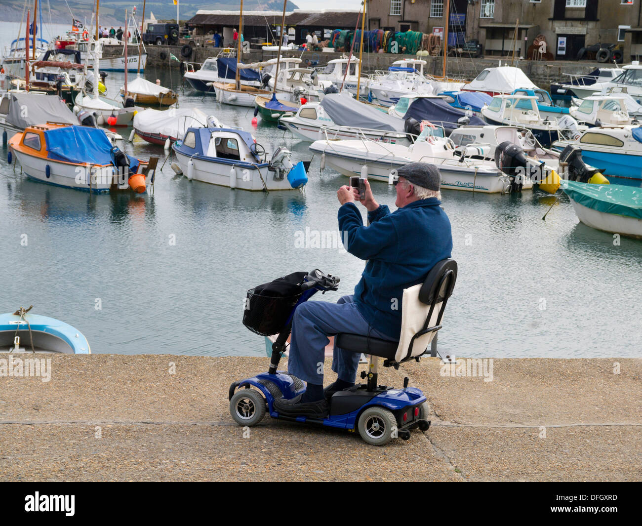 Un uomo su uno scooter di mobilità di scattare una foto, Lyme Regis, Dorset, Inghilterra. Foto Stock
