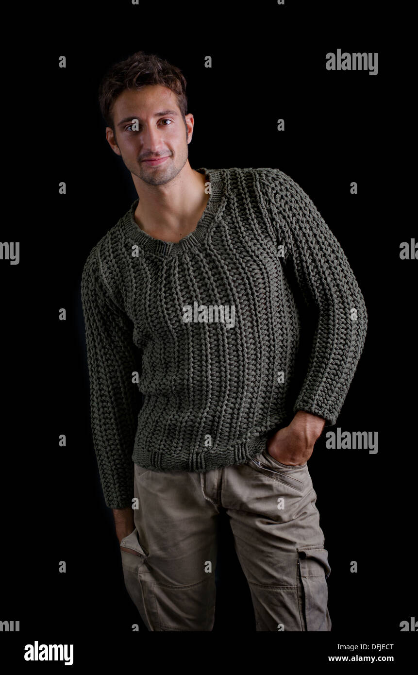 Attraente e fiducioso giovane uomo che indossa maglione sorridente, isolato su nero Foto Stock