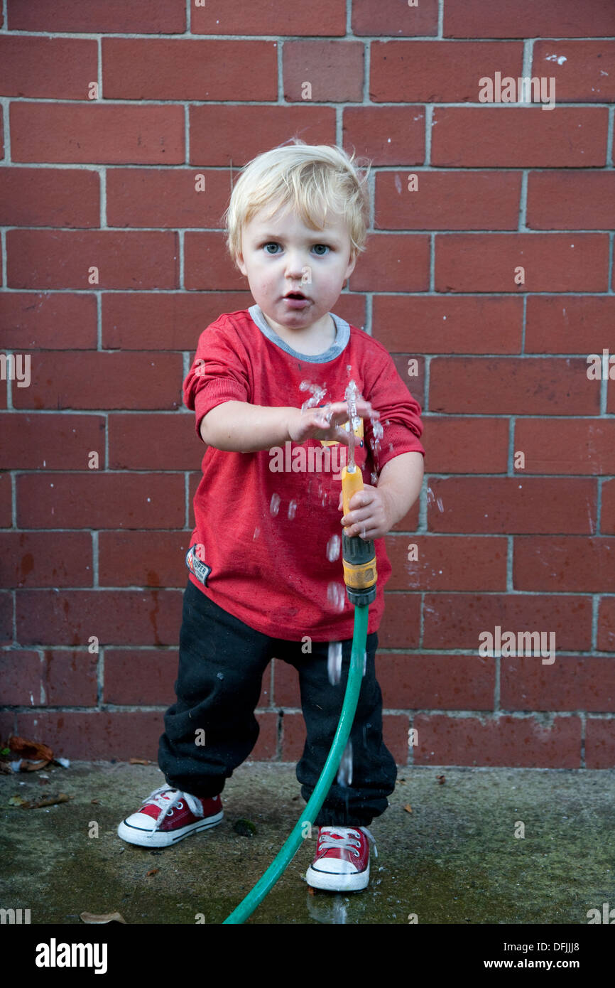 Il Toddler giocare all'aperto e con un tubo flessibile Foto Stock