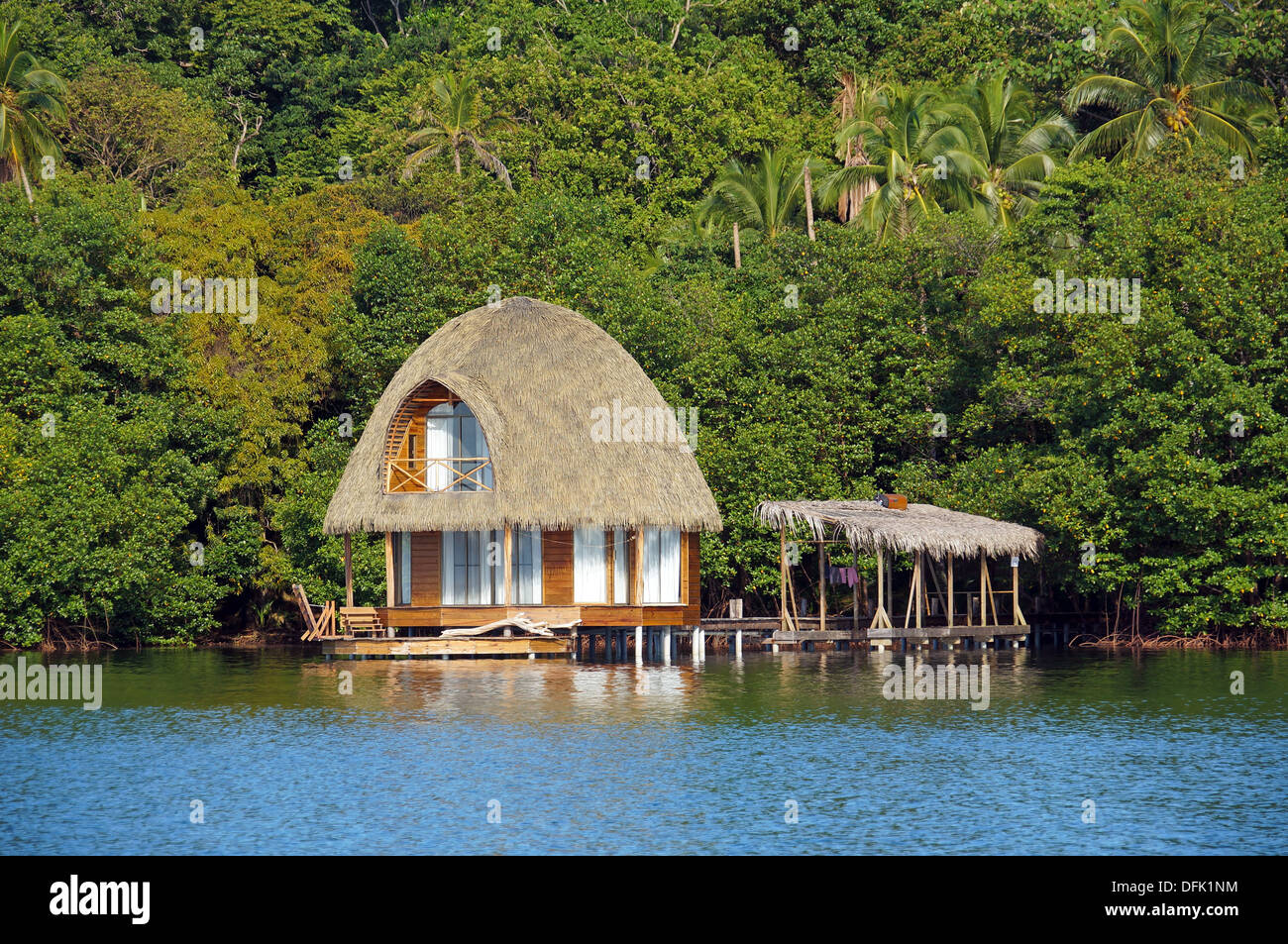 Over water bungalow con tetto di Palm e la lussureggiante vegetazione tropicale in background, Bocas del Toro, Mar dei Caraibi, Panama Foto Stock