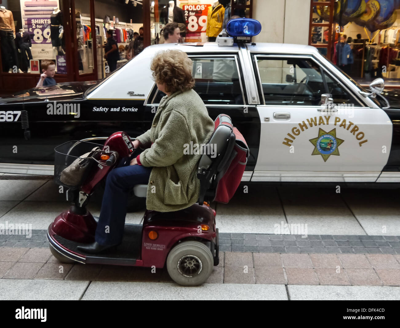 Un senior lady in una mobilità mobile passa su un California Highway Patrol auto della polizia. Foto Stock