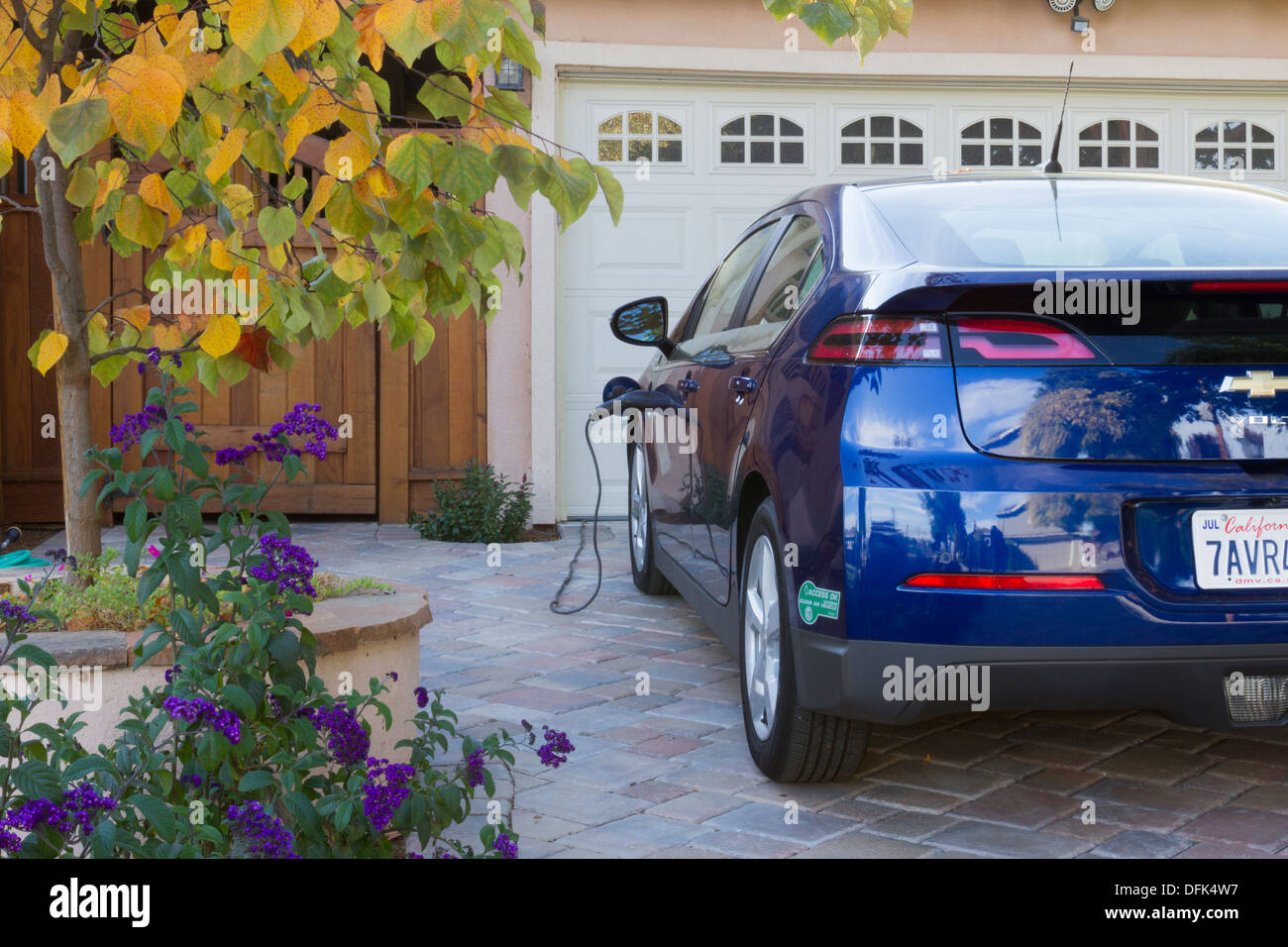 Plug-in auto elettrica con adesivo carpool parcheggiato nel viale di accesso con il connettore collegato alla presa di corrente e caricare a casa Foto Stock