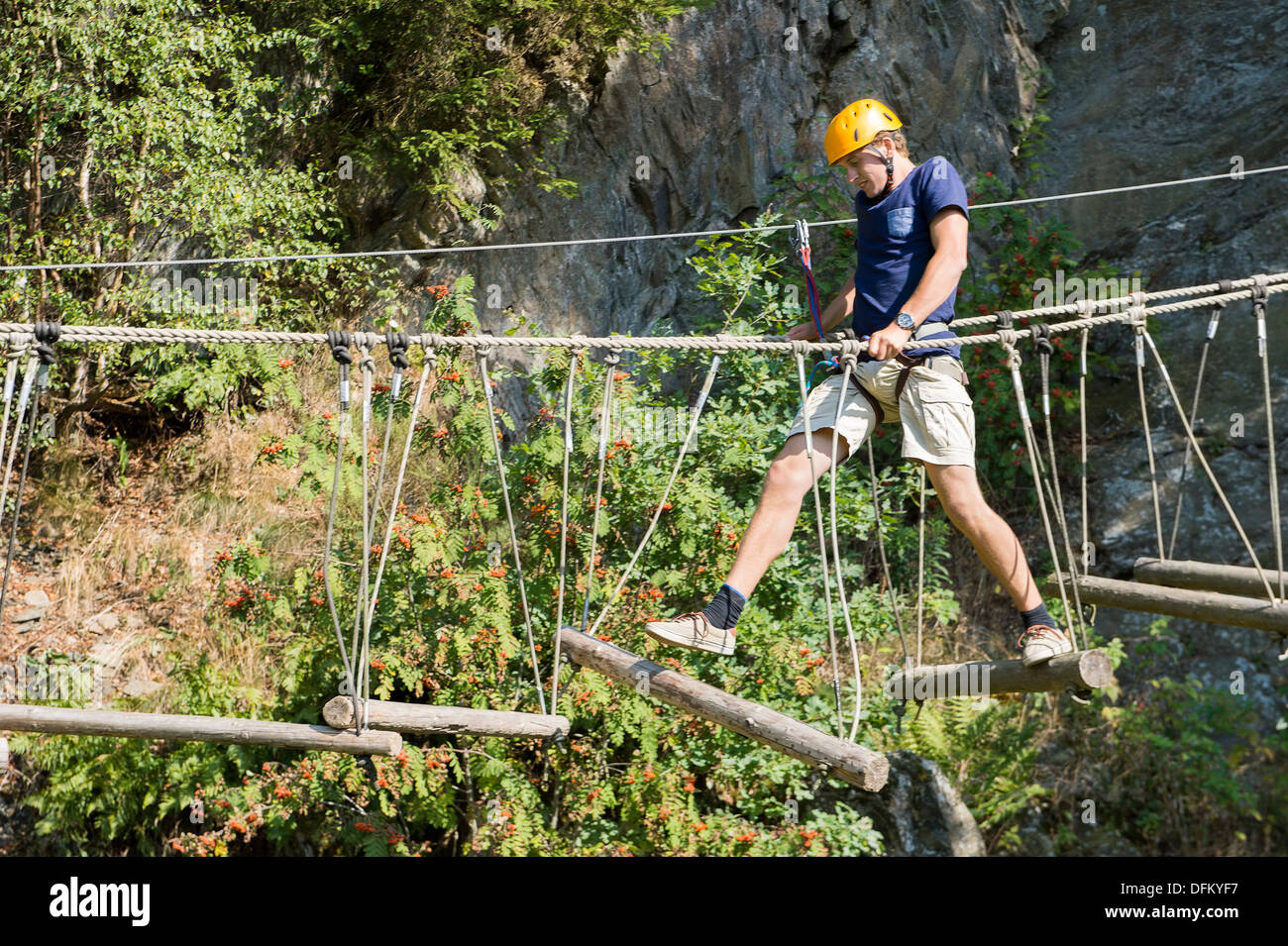 Giovane uomo attraversando il ponte di albero, vincendo la sua paura delle altezze Foto Stock