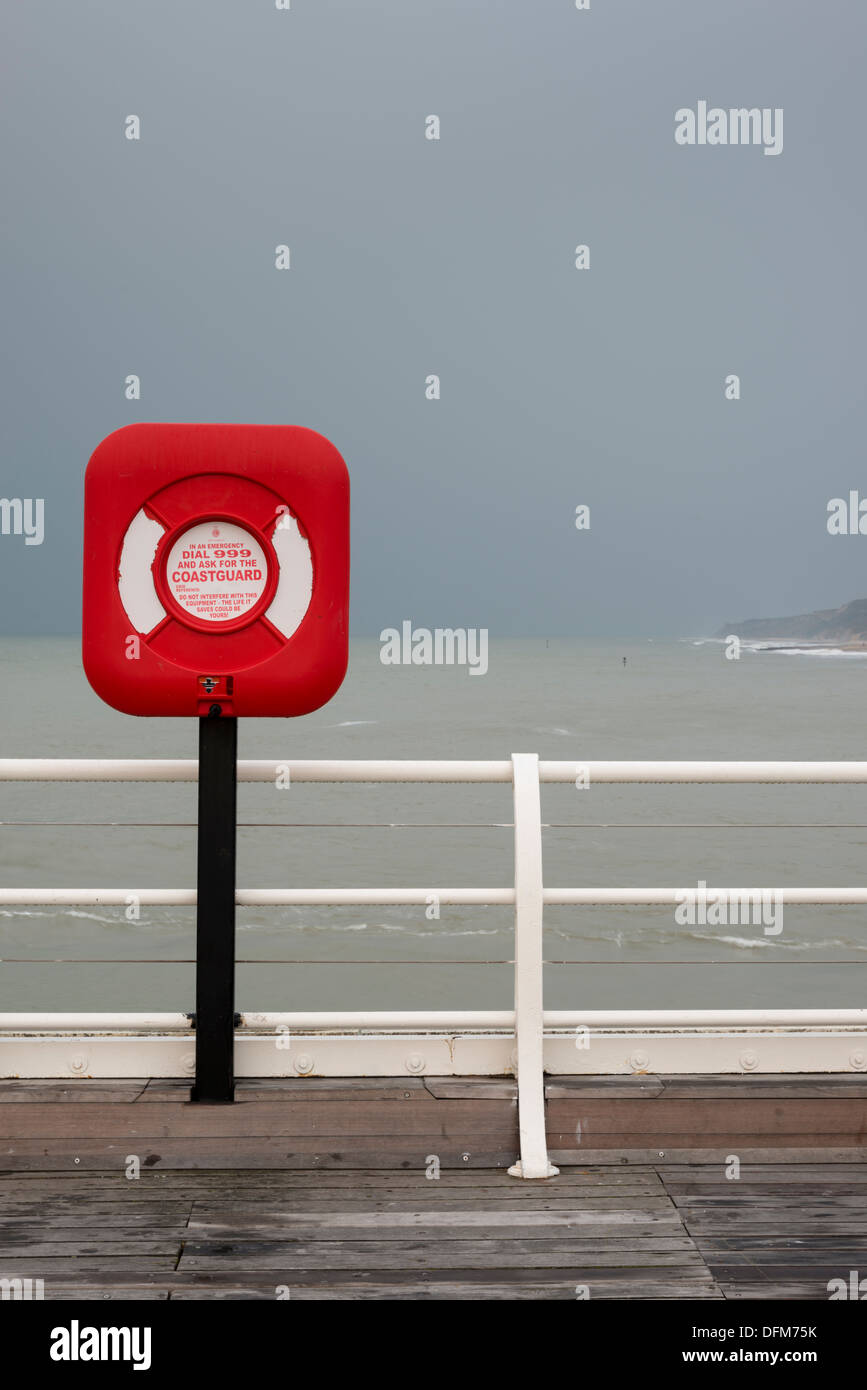 Un lifebouy su Cromer Pier NORFOLK REGNO UNITO nella cortina di nubi di luce con forte rosso saturo di colori Foto Stock