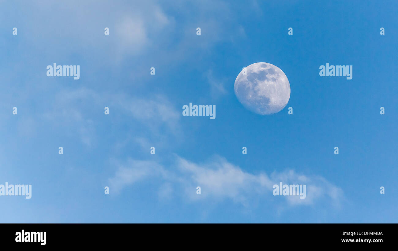 Una immagine della luna durante il giorno con un chiaro cielo blu e nuvole in background Foto Stock