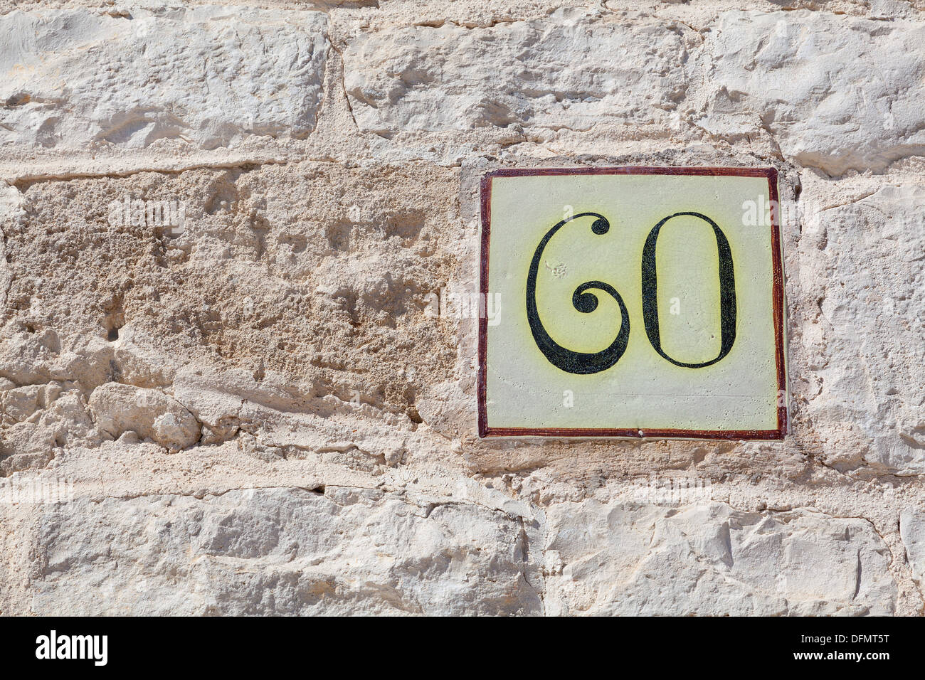 Numero sessanta su una piastrella attaccato al muro di pietra Foto Stock