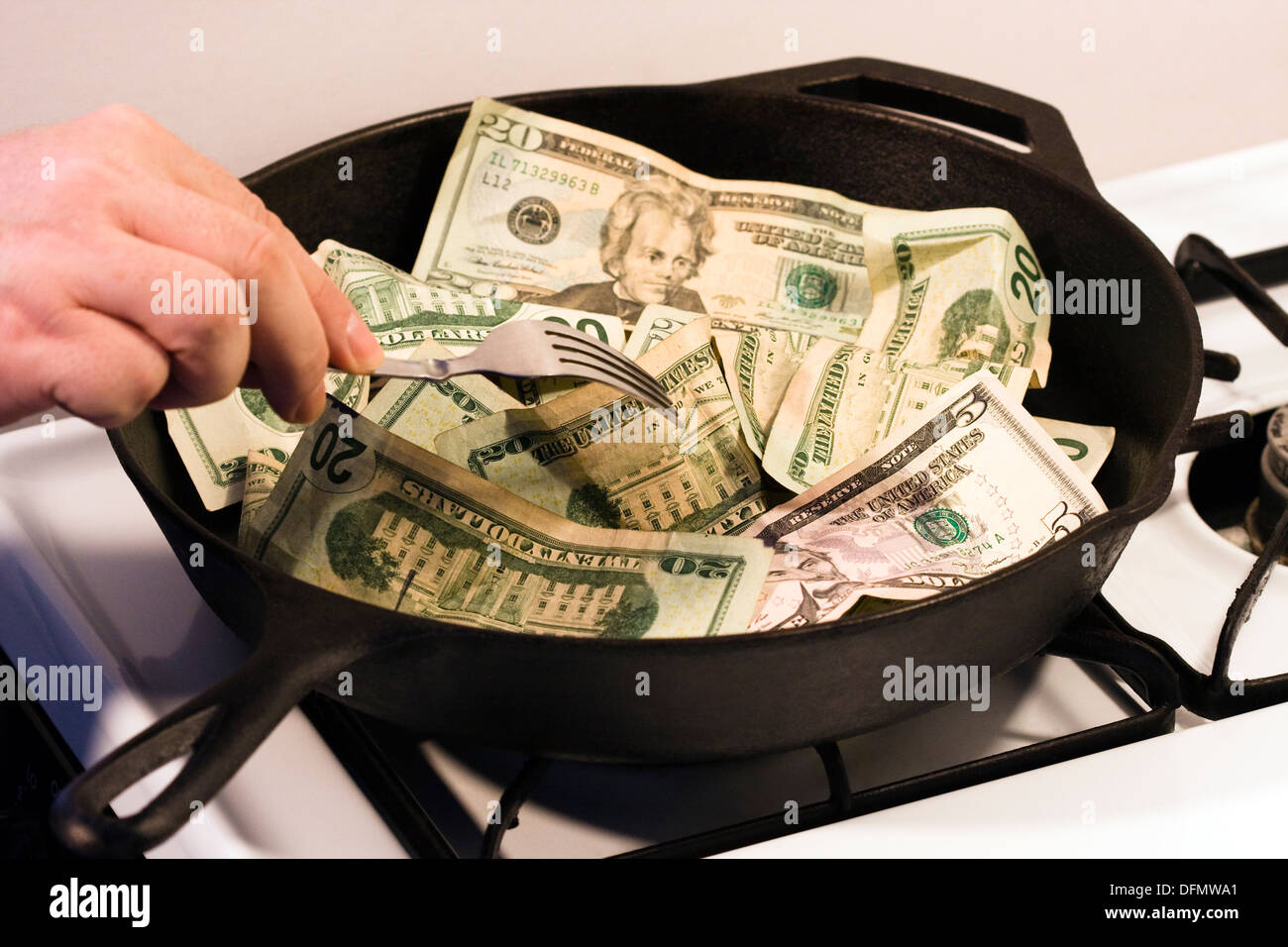 Mano d'uomo con la forcella su un 12' in ghisa pesante padella sulla combustione di gas di stufa riempita con denaro. Foto Stock