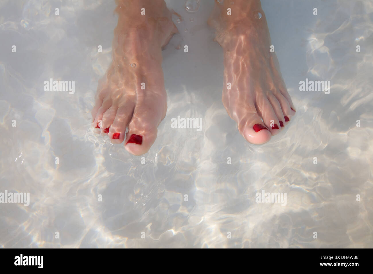 Le dita dei piedi dipinte di rosso in una piscina di acqua. Foto Stock