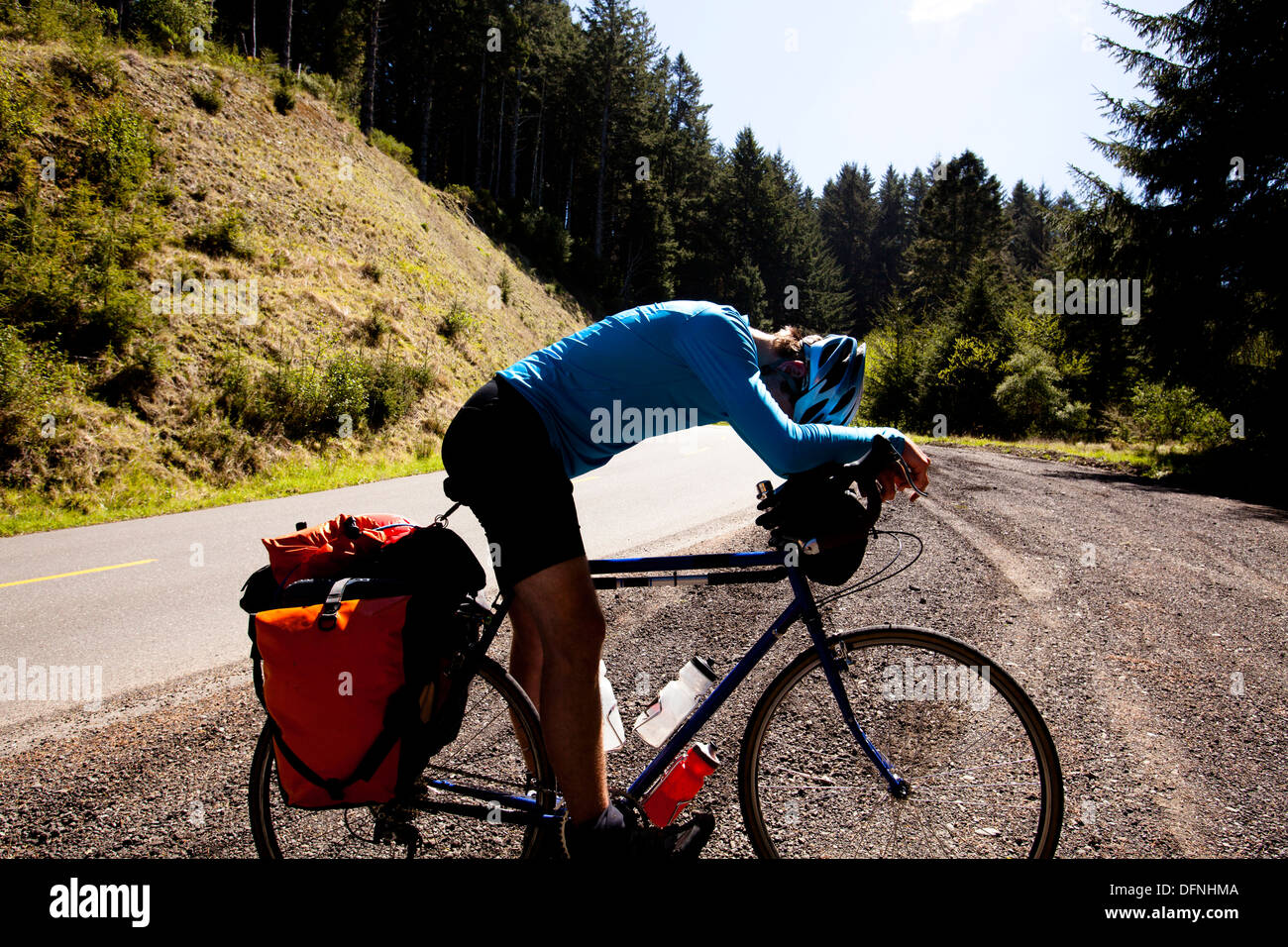 Un maschio esausto ciclista si appoggia sopra la sua touring bike mentre alpinismo Mattole Road vicino a Ferndale, California. Foto Stock