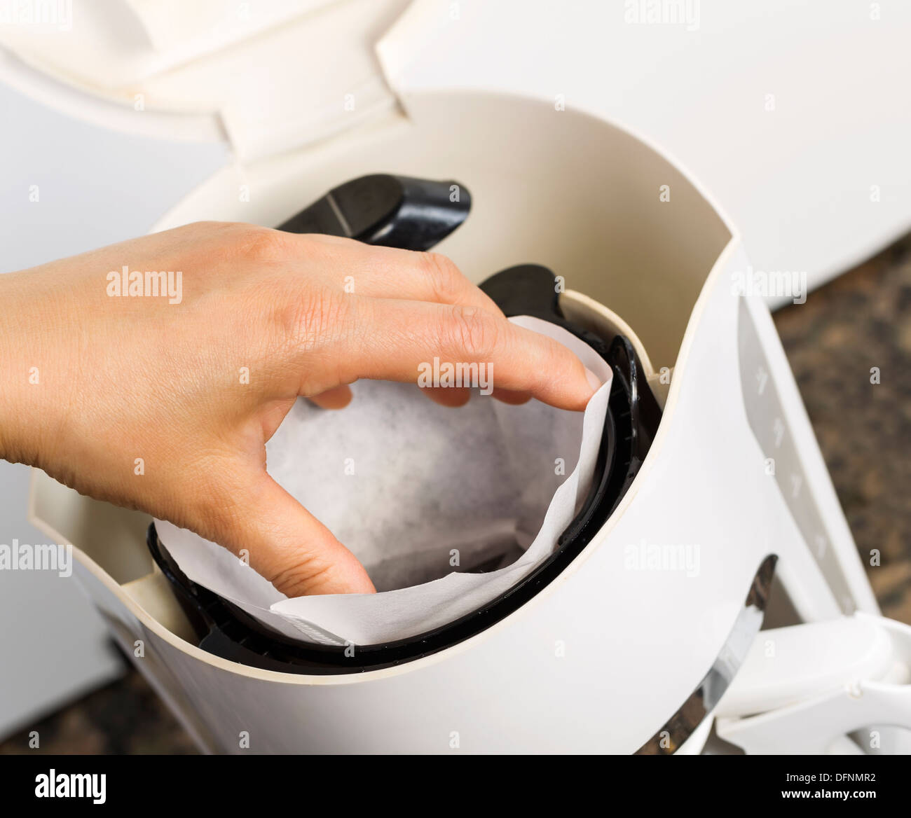 Foto angolata di mano femminile mettendo in bianco sbiancato filtro per caffè con caffè e cucina in pietra bancone in backgrou Foto Stock