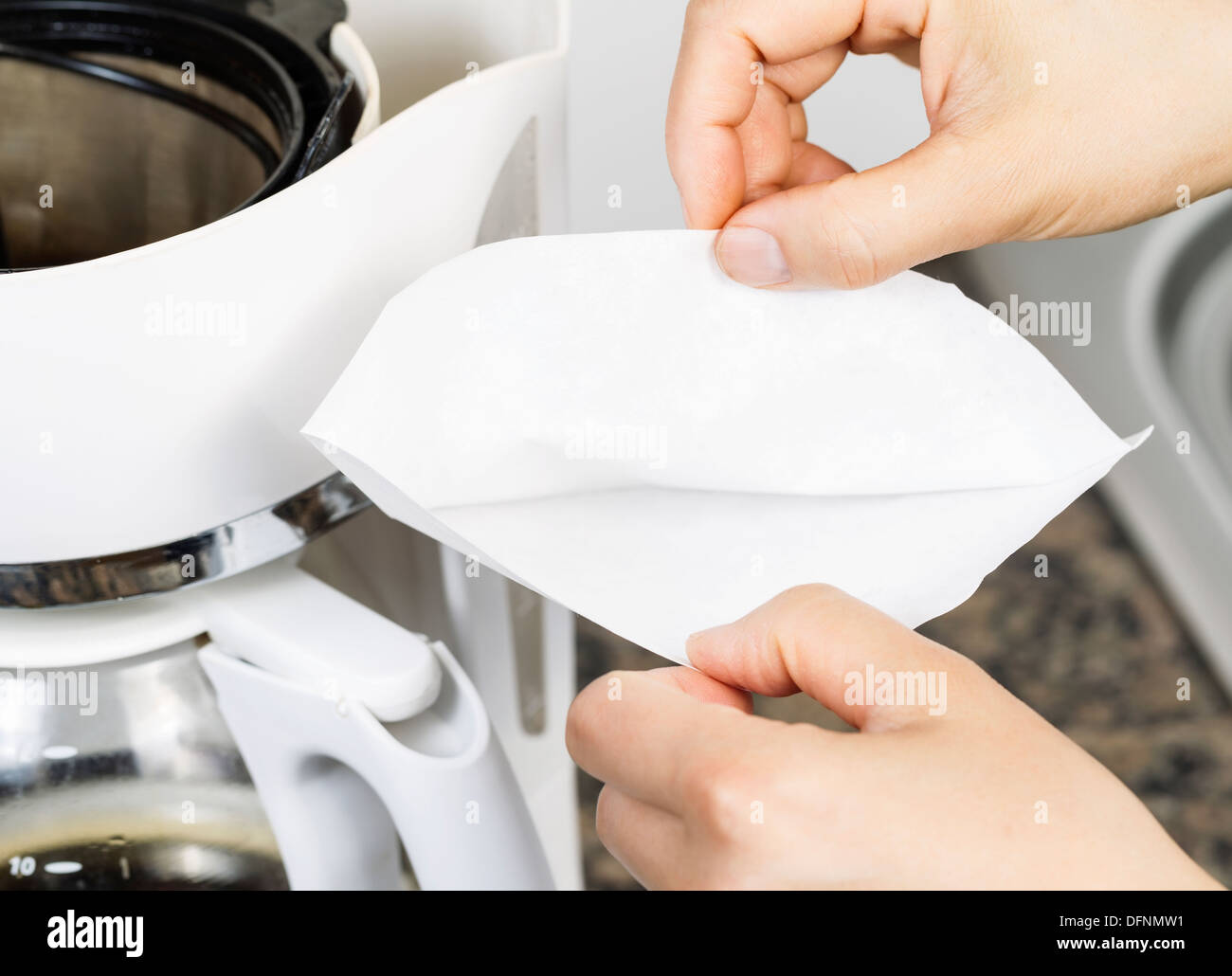 Foto orizzontale della femmina di apertura a mano bianca sbiancata filtro per caffè con caffè, pietra bancone cucina top e lavabo Foto Stock