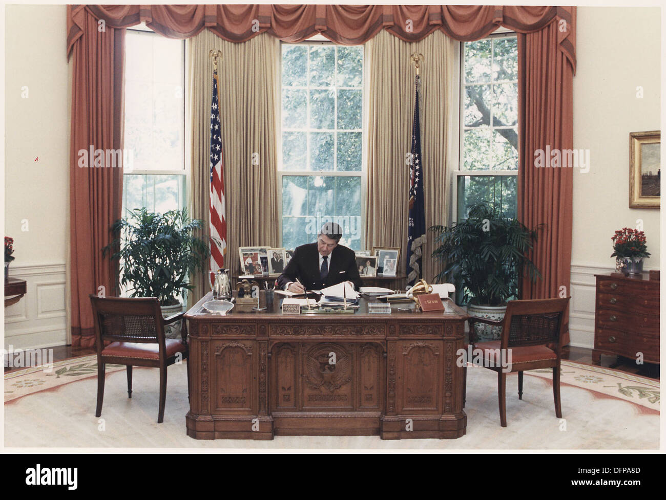 Questa foto mostra il presidente Ronald Reagan che lavora alla sua scrivania nell'ufficio ovale. Preso nel 1985, riflette i doveri presidenziali di Reagan e offre uno sguardo sull'ambiente di lavoro del presidente degli Stati Uniti durante il suo mandato. Foto Stock