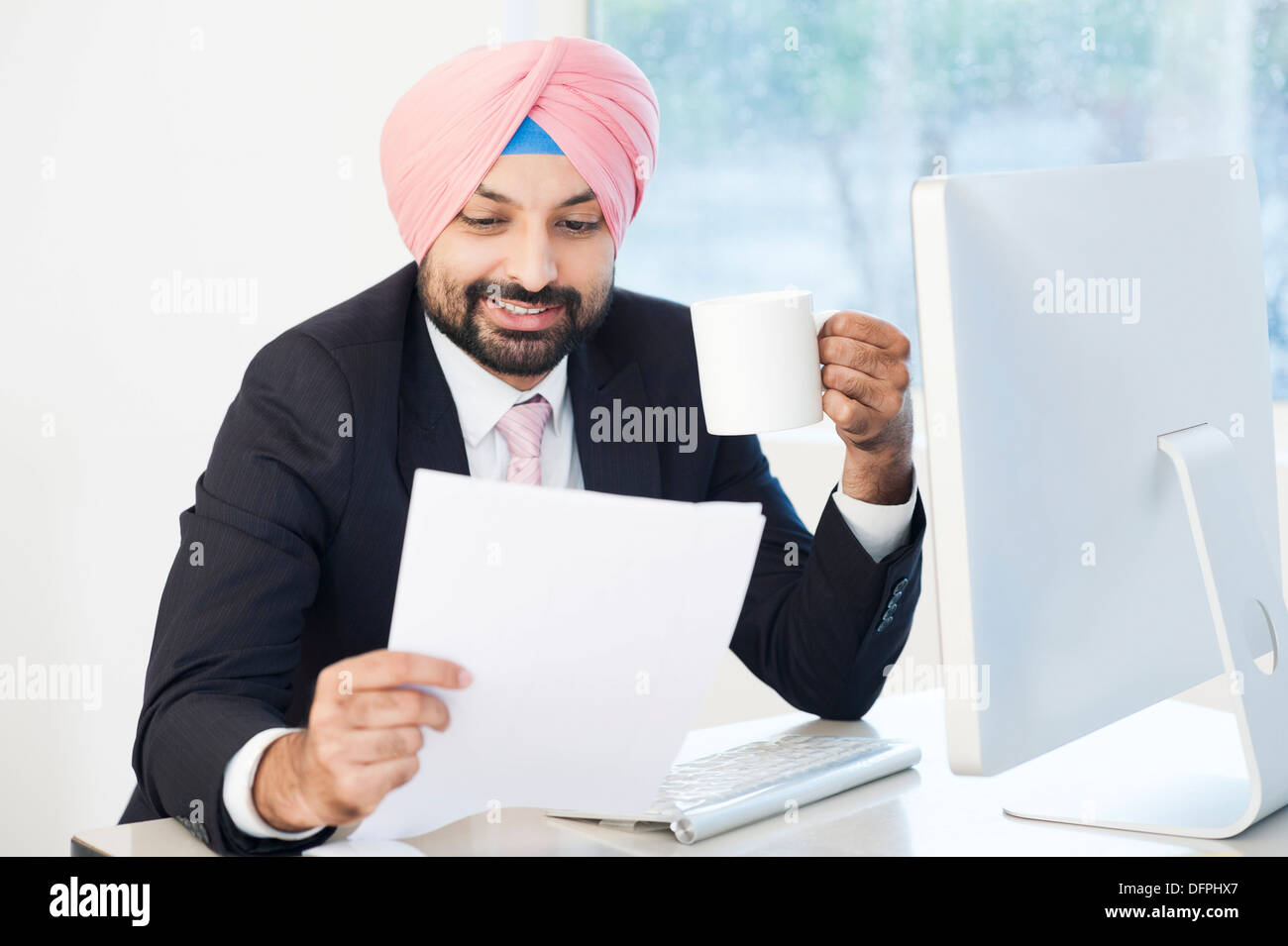 Imprenditore a bere caffè e alla ricerca di un documento in un ufficio Foto Stock