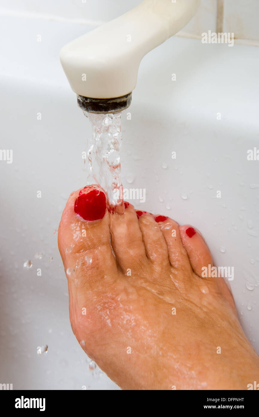 Una donna sta mantenendo il suo piede sotto il caldo di acqua calda del rubinetto del bagno Foto Stock