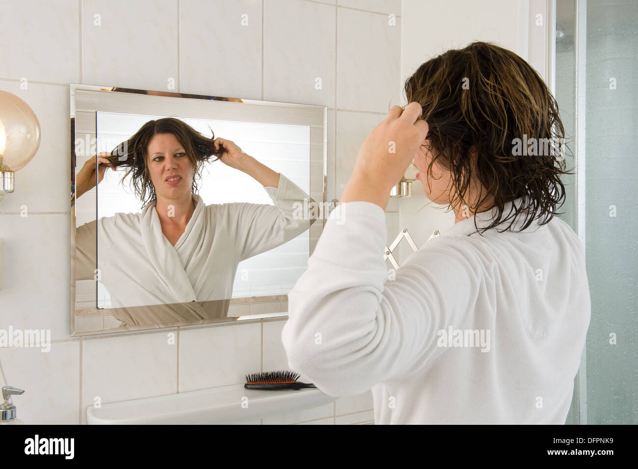Una donna sta guardando nello specchio del bagno e avente un 'bad hair day". Foto Stock