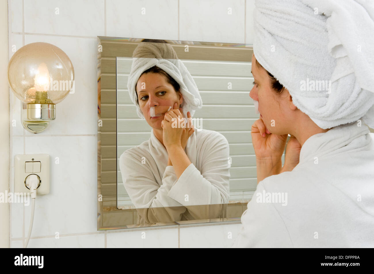 Una donna è la depilazione i piccoli peli dai suoi baffi davanti a uno specchio Foto Stock