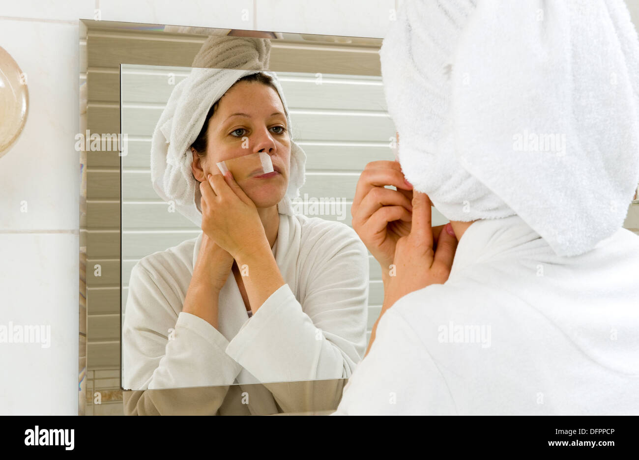 Una donna è la depilazione i piccoli peli dai suoi baffi davanti a uno specchio Foto Stock