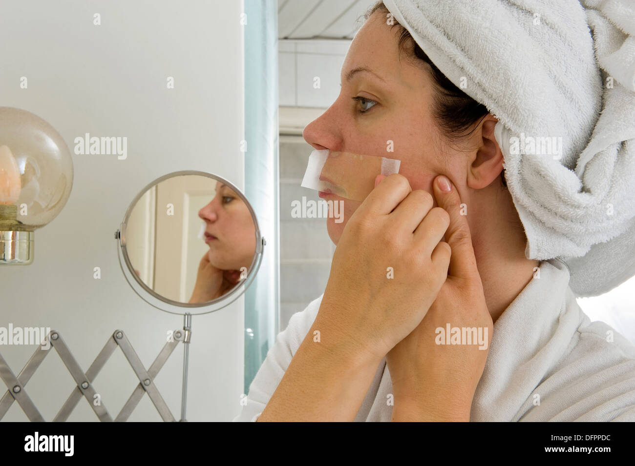 Una donna è la depilazione i piccoli peli dai suoi baffi davanti a uno specchio Foto Stock