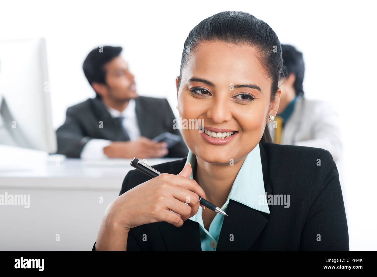 Imprenditrice sorridente in ufficio con i loro colleghi in background Foto Stock