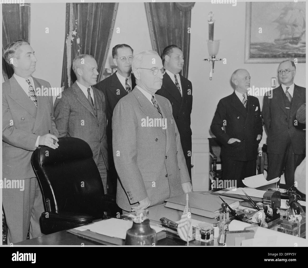 Il presidente Harry S. Truman è fotografato in piedi alla sua scrivania nell'ufficio ovale, con membri del suo Gabinetto nelle vicinanze, che riflettono la natura formale e collaborativa del processo decisionale presidenziale. Foto Stock