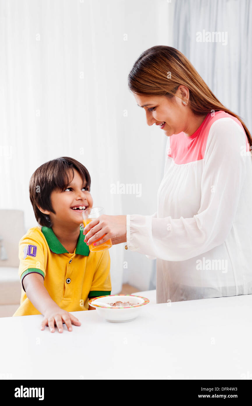 Donna sorridente succo di alimentazione a suo figlio Foto Stock