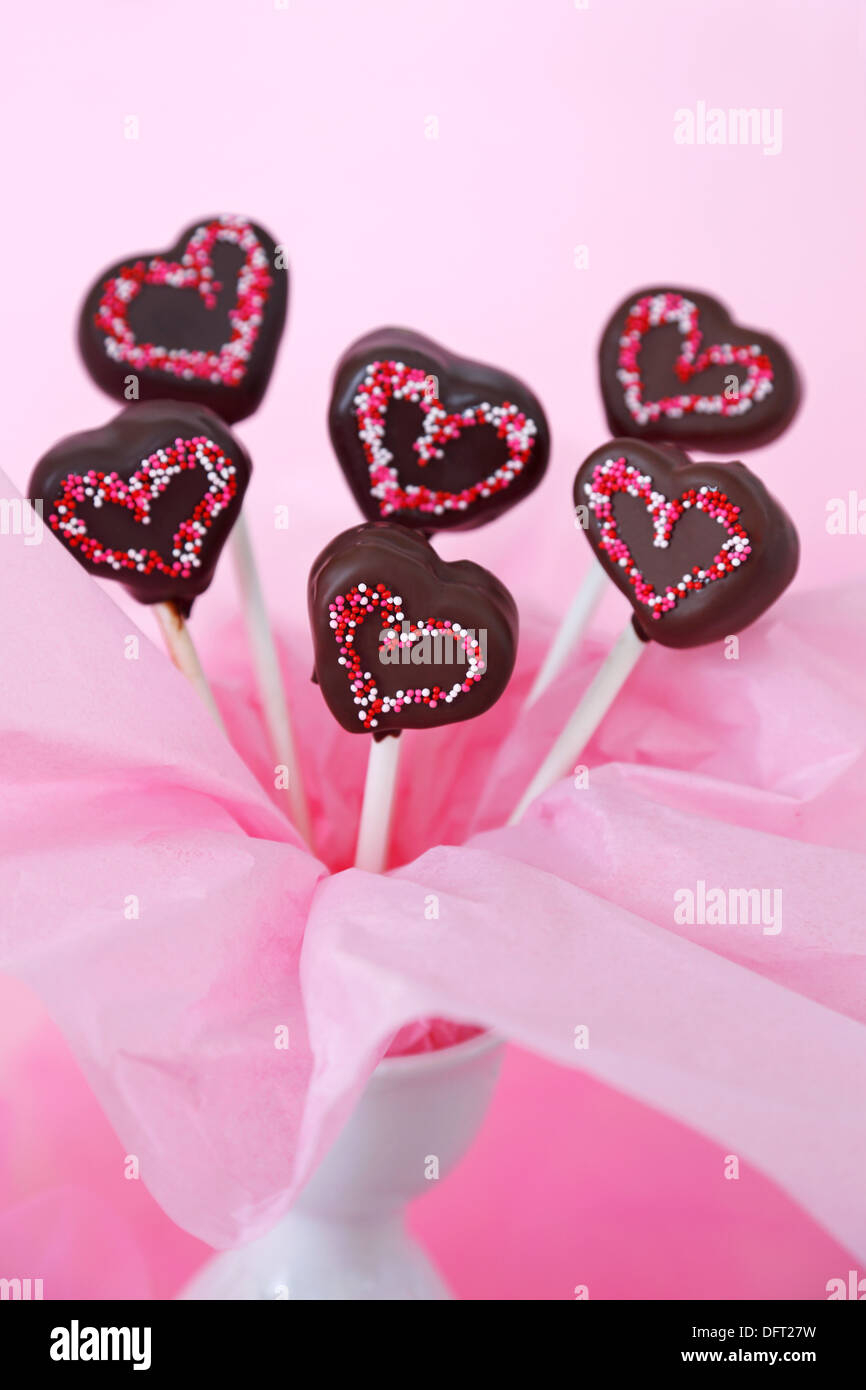 Al cioccolato a forma di cuore immerso cake pops con spruzza su uno sfondo rosa Foto Stock