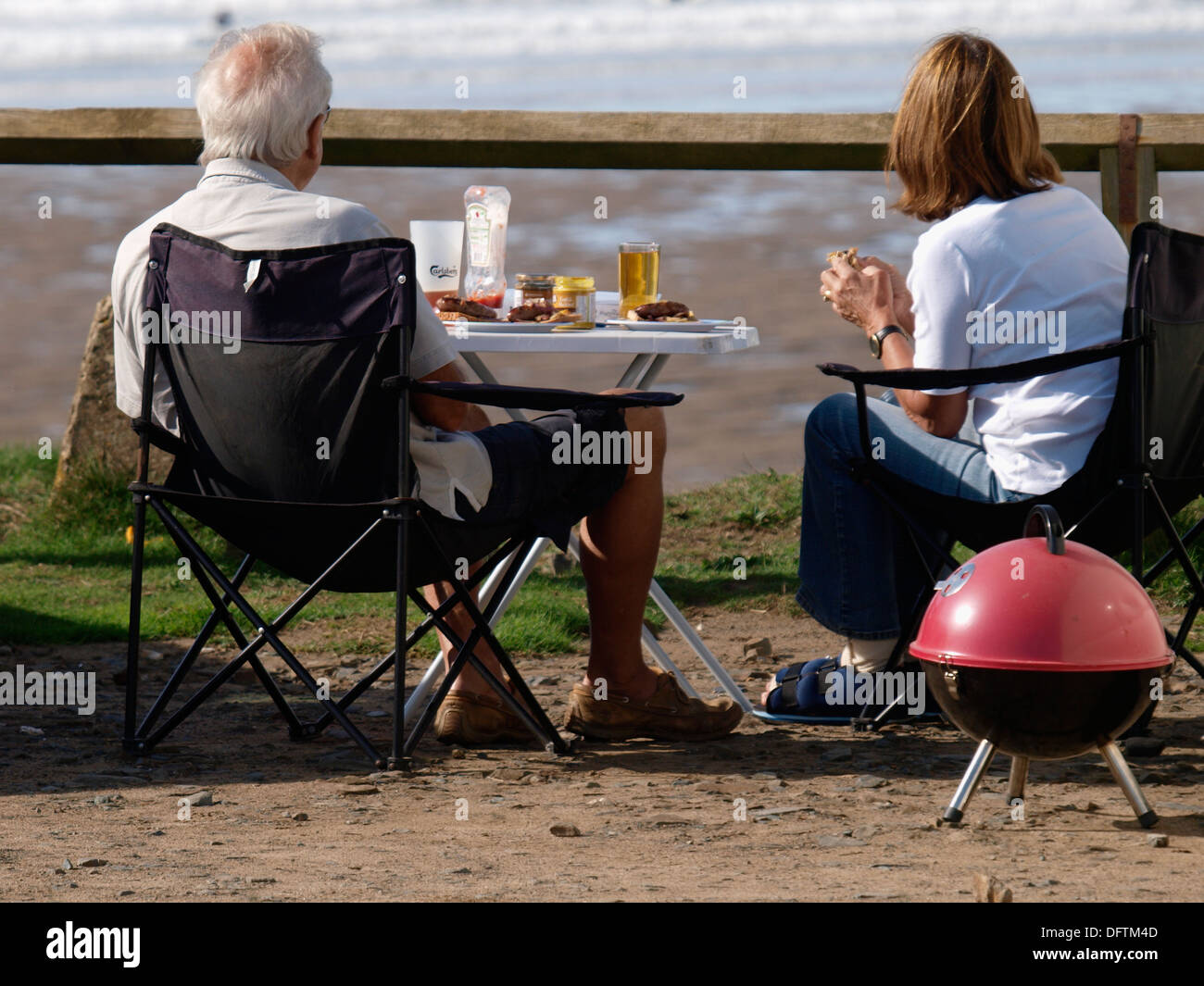 Coppia matura avente un barbeque sulla scogliera che si affaccia sulla spiaggia, Widemouth Bay, Cornwall, Regno Unito Foto Stock