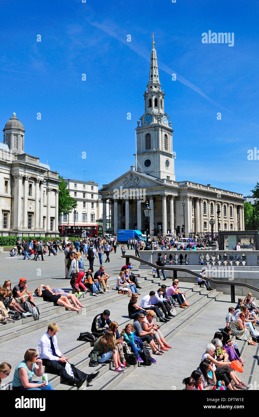 Londra, Inghilterra, Regno Unito. Trafalgar Square - la gente seduta sulle fasi di sun. Chiesa di St Martin nei campi Foto Stock
