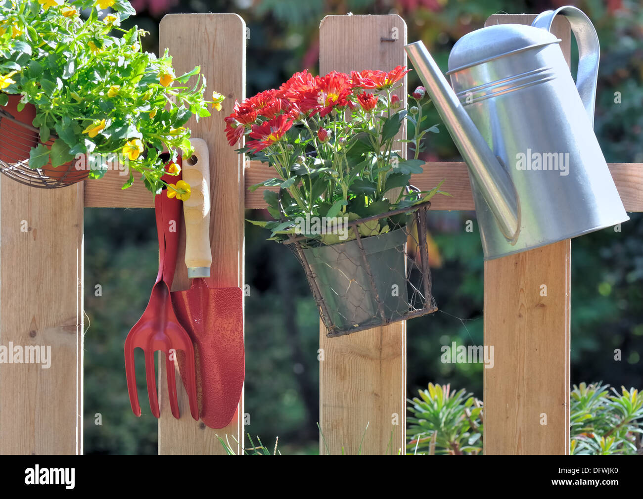 Utensili da giardinaggio e vaso di fiori appesi su una recinzione Foto Stock