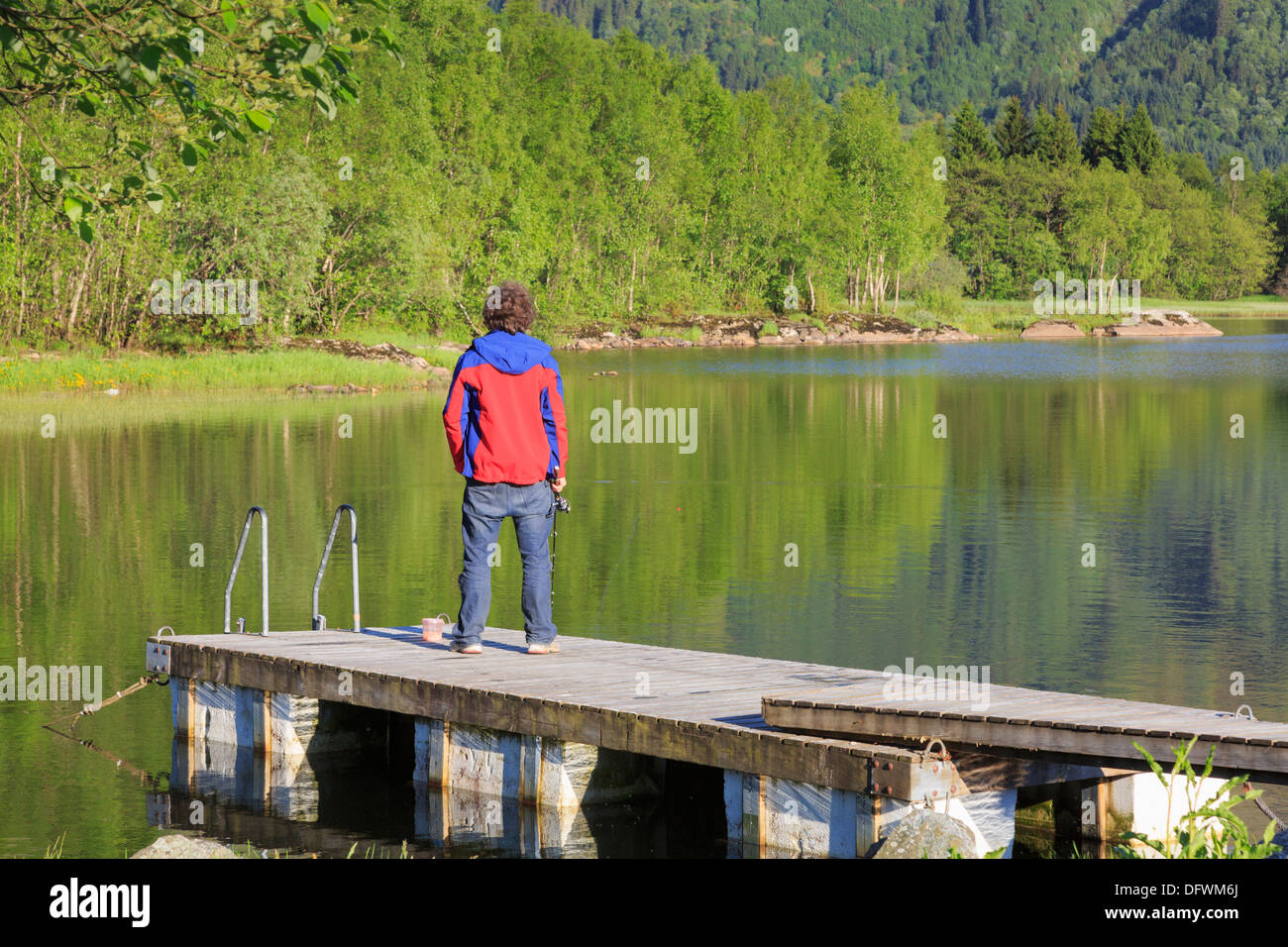 Un uomo solo di pesca da un pontile in legno nel lago Haukeland in estate vicino a Bergen Hordaland county, Norvegia e Scandinavia Foto Stock