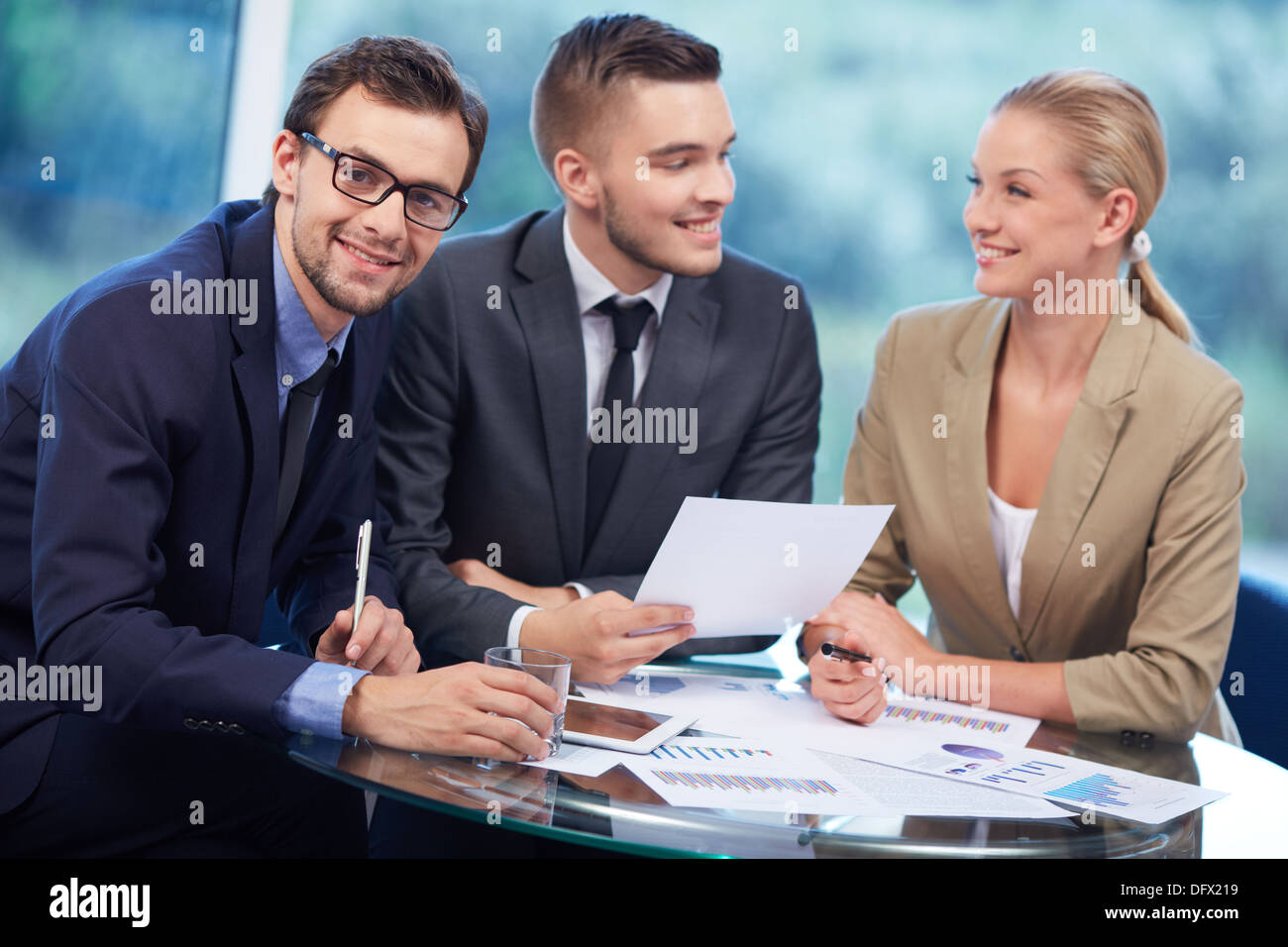 Imprenditore di successo guardando la fotocamera al lavoro mentre il suo partner discutere le idee sullo sfondo Foto Stock