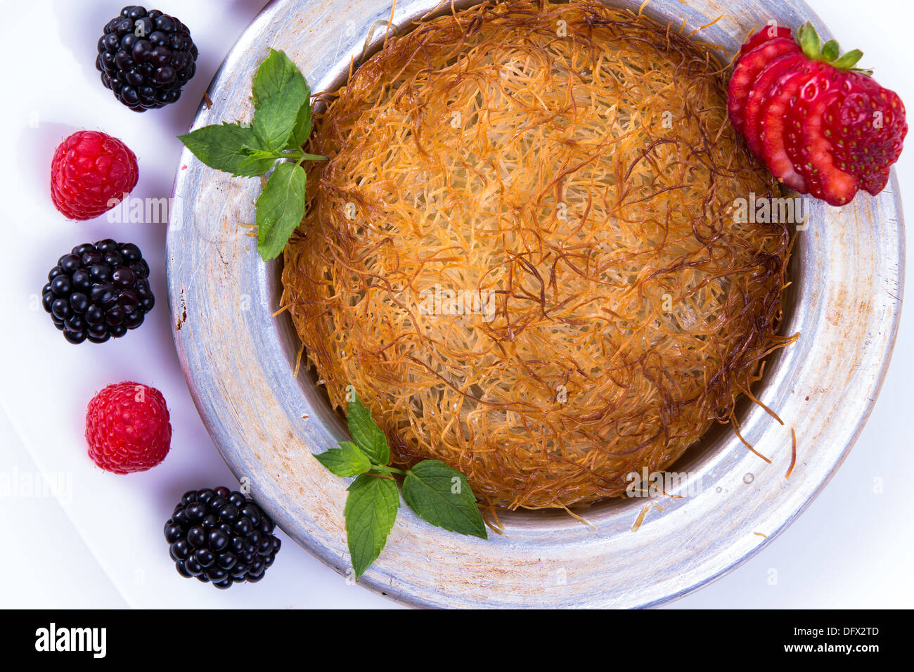 Dolce turco kunefe servita su una piastra bianca con zecche e fragole a fette lungo frutti rossi e neri Foto Stock