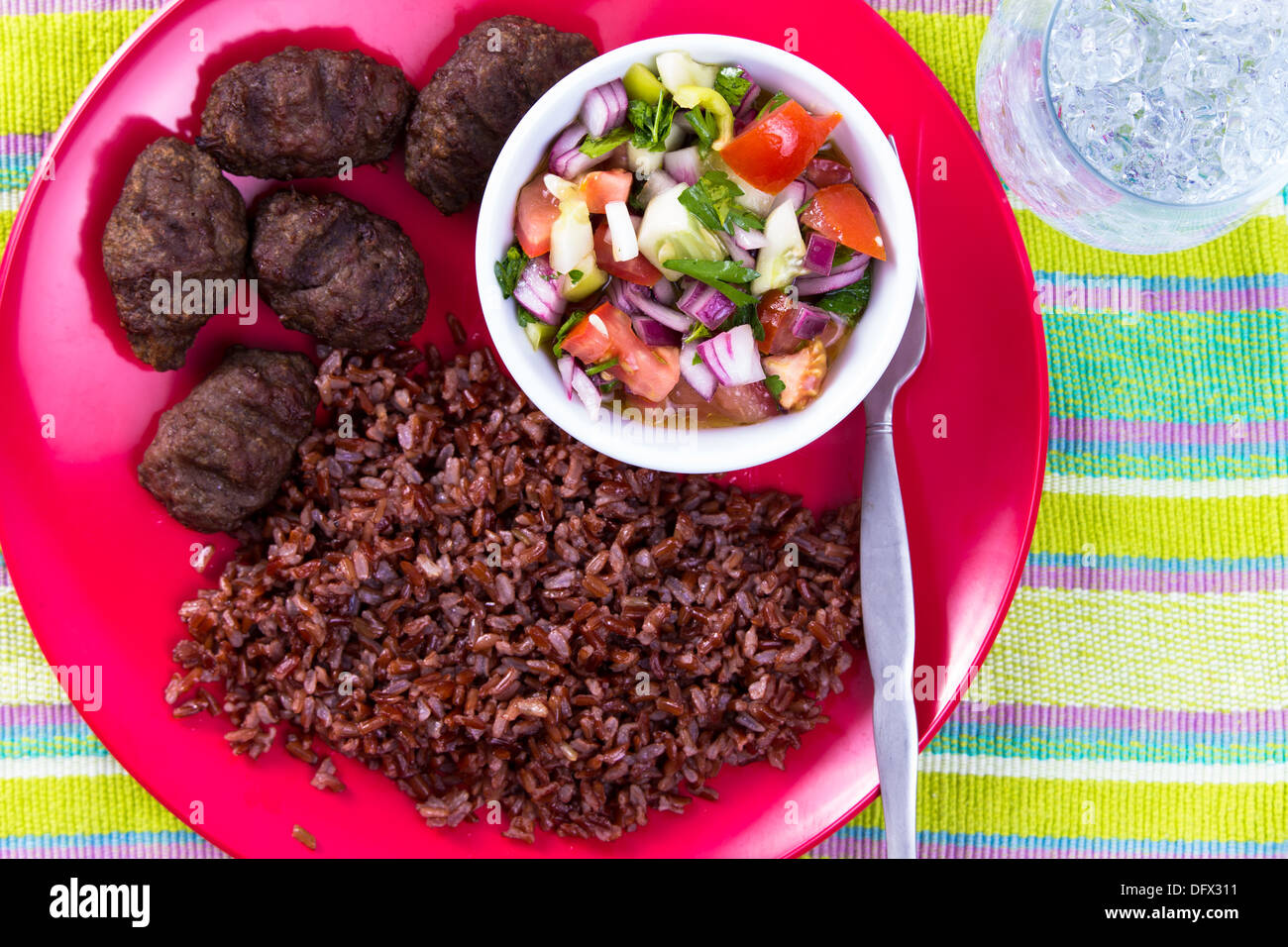 Bagno turco polpettine di carne Kofte servita con il rosso il riso pilaf e turco insalata Shepperd su una targhetta rossa lungo con acqua ghiacciata. Foto Stock