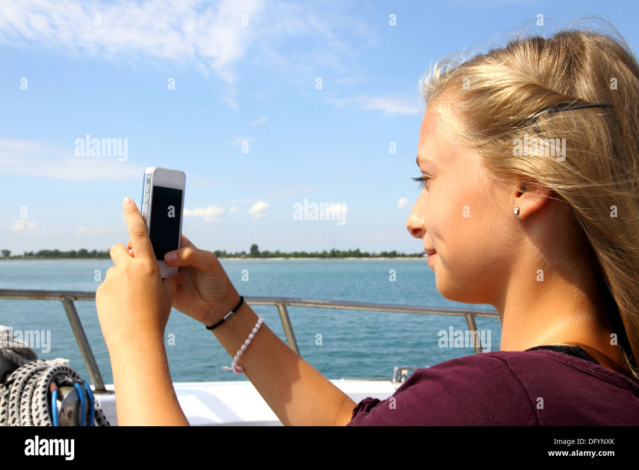 Sorridente ragazza bionda con il telefono sulla nave, orizzontale Foto Stock