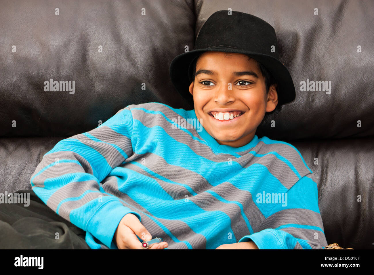 Un felice ragazzo giovane con un grande sorriso sporting un nero fedora, sdraiati su un divano in pelle nera Foto Stock