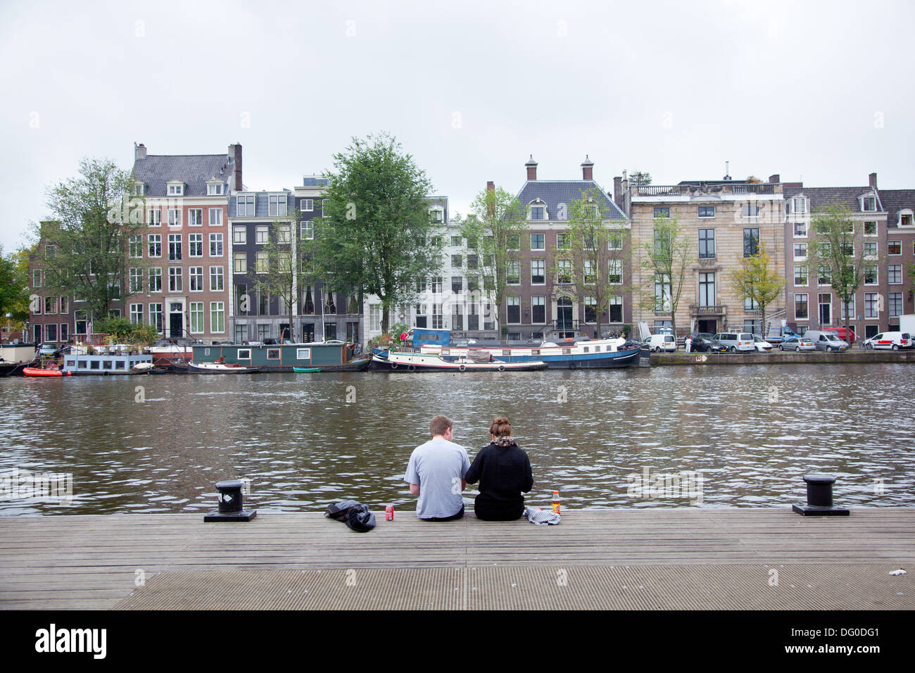 Due giovani turisti picknick lungo gli argini del fiume Amstel di Amsterdam Foto Stock