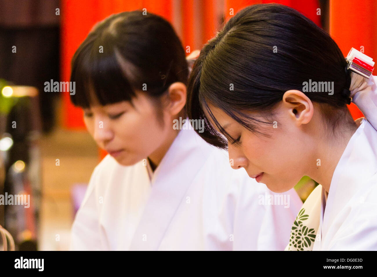 Primo piano, 2 giovani miko, Shinto santuario nubile, al santuario di Ikuta a Kobe durante le celebrazioni di Capodanno. Entrambi guardando verso il basso qualcosa di inosservato. Foto Stock