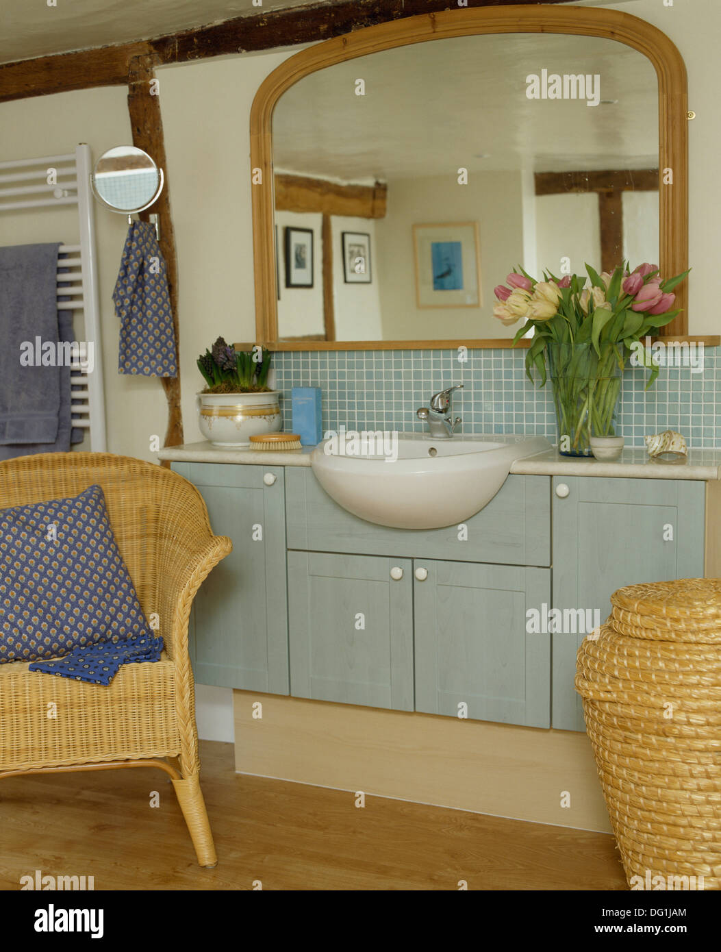 Legno grande-specchio incorniciato suddetto bacino in blu pallido montato vanity in cottage bagno con sedia in vimini e 'Ali Baba' cestello Foto Stock