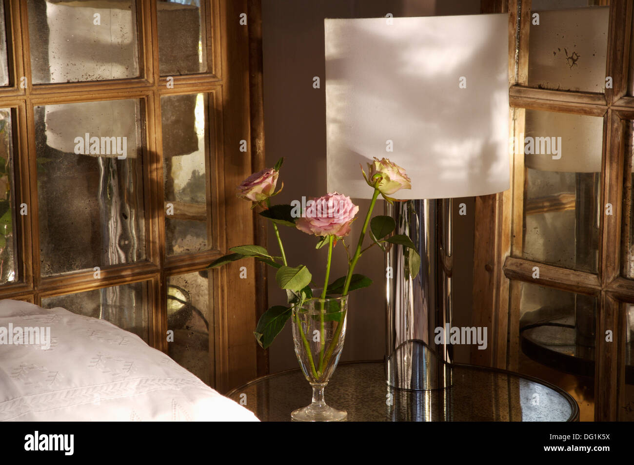 Close up di rose rosa in vaso di vetro accanto a lampada bianca sul comodino di fronte all interno delle porte in vetro Foto Stock