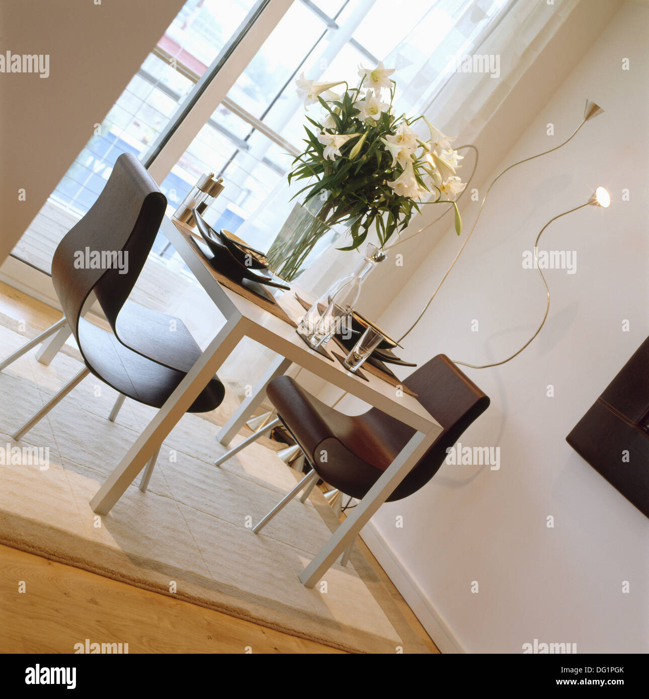 Vaso di gigli bianchi sul tavolo con sedie nere nella sala da pranzo del moderno appartamento di città con crema tappeto sul pavimento in legno Foto Stock