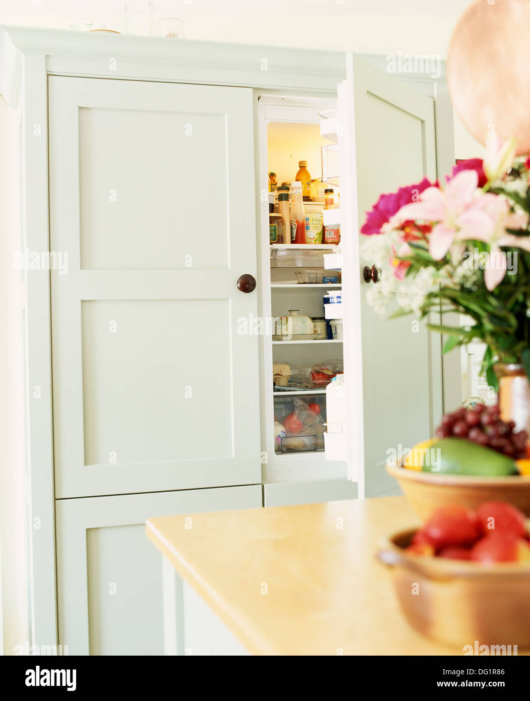 Vaso di fiori e ciotole di frutta sul tavolo in cucina di paese con la porta aperta ad un tenue blu grigio equipaggiato Frigo Foto Stock