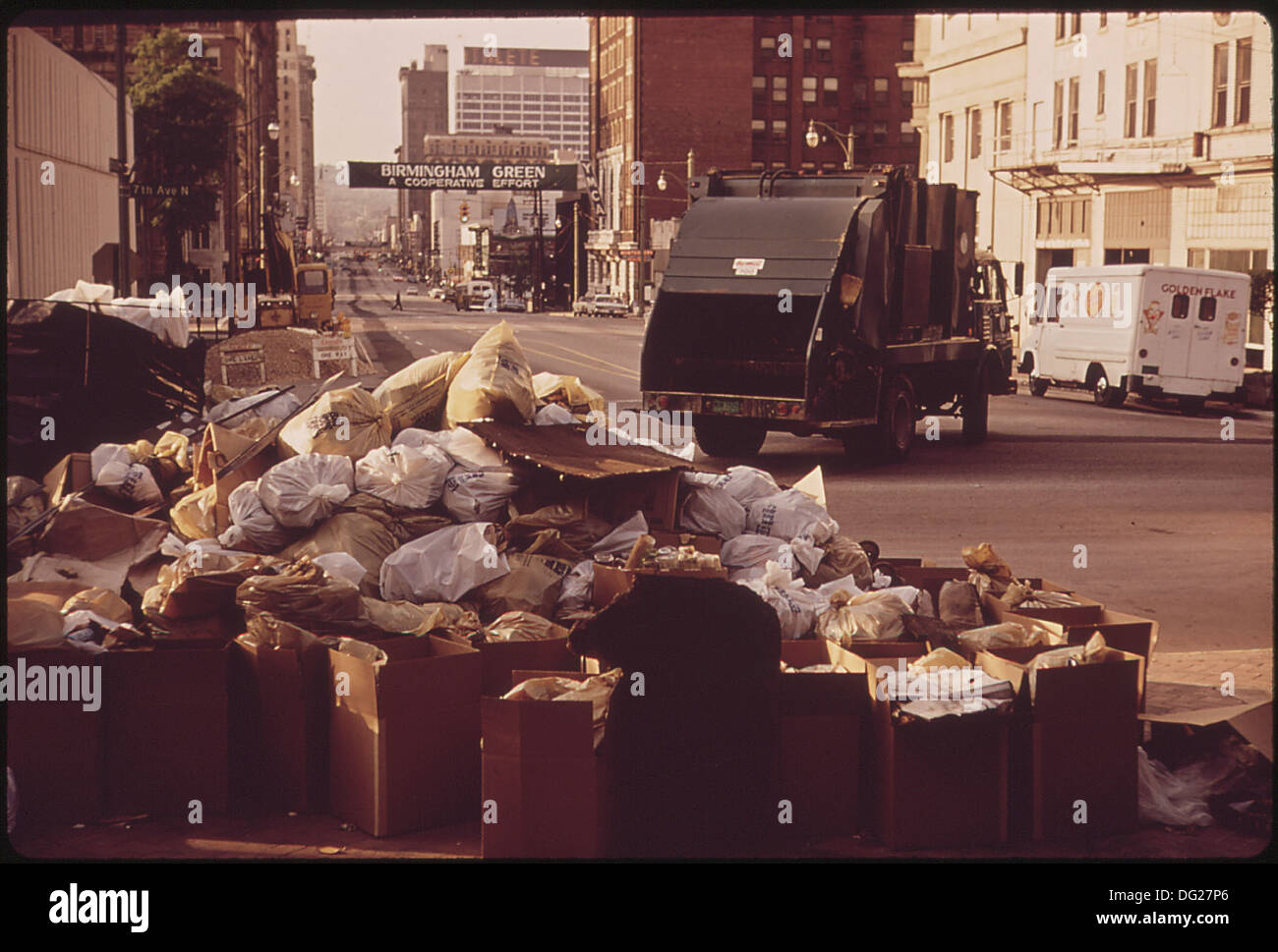 Un camion del reparto di sanificazione si prepara a trasportare rifiuti stradali accumulati, con uno striscione che ricorda ai cittadini le responsabilità di gestione dei rifiuti. Foto Stock