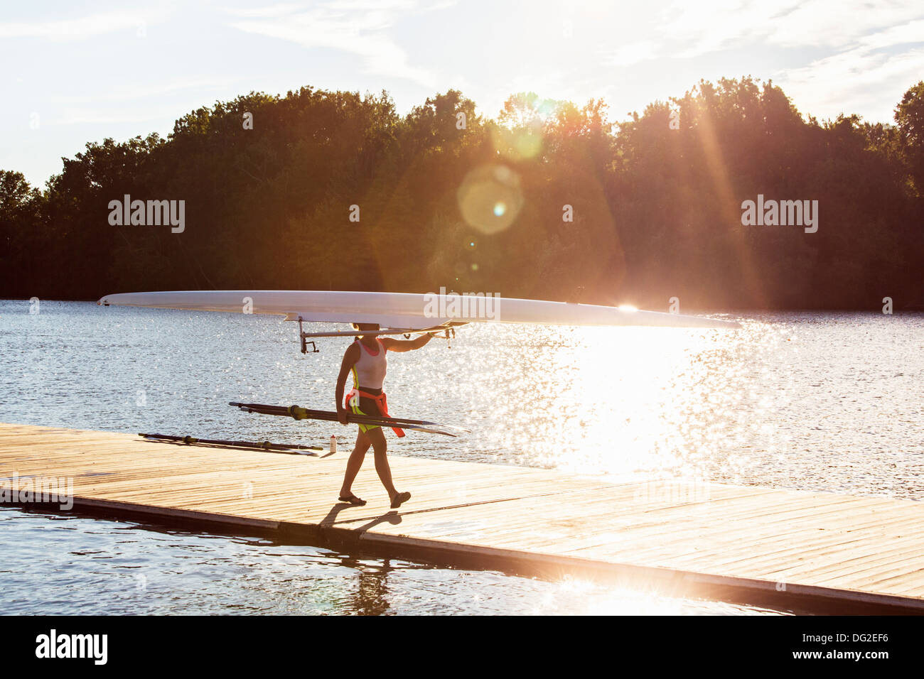 Donna vogatore con guscio in barca a piedi su un molo di sunrise Foto Stock