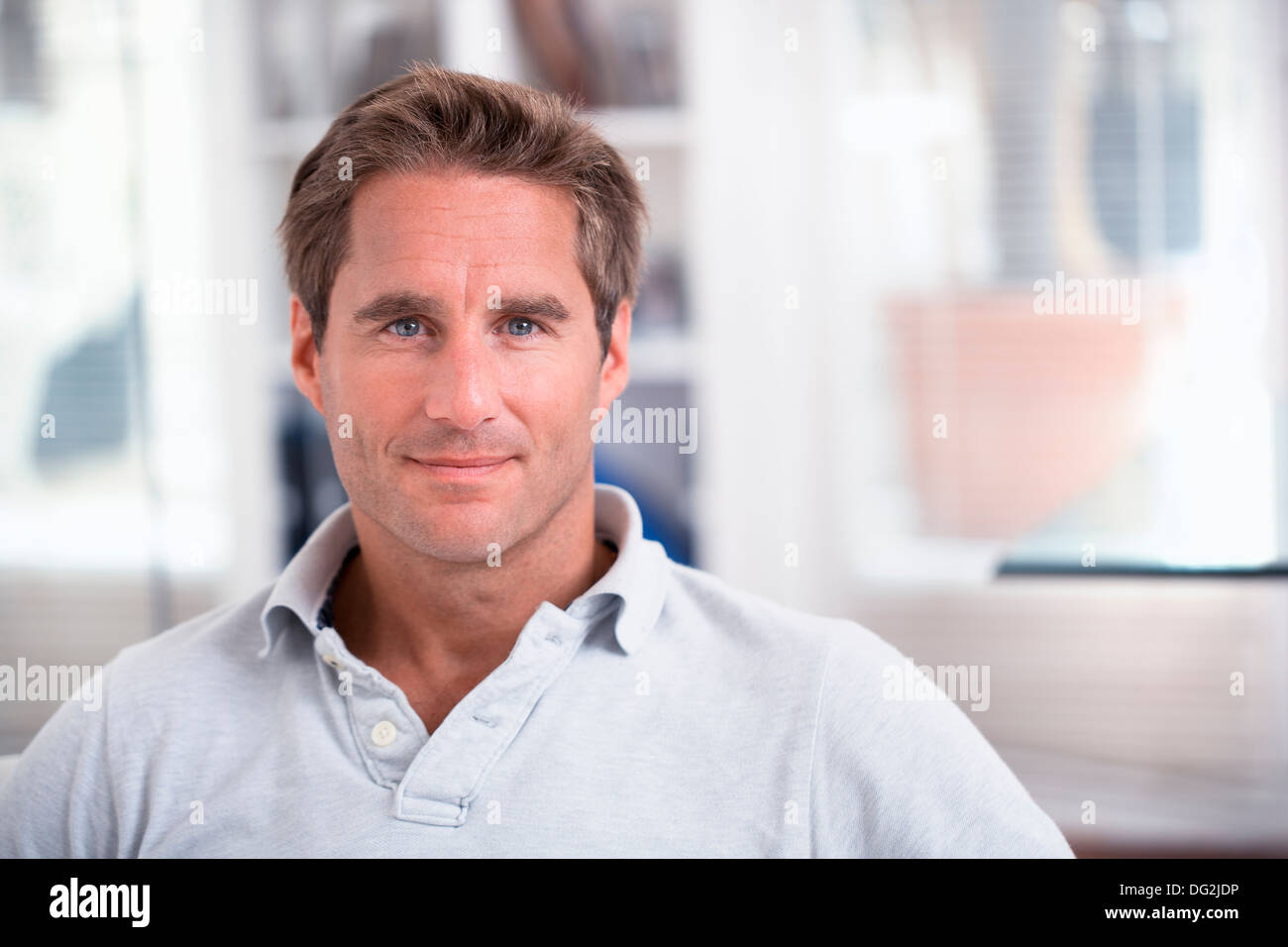 Voce maschile seduto sul divano in un momento di relax a casa cercando di fotocamera a sorridere Foto Stock