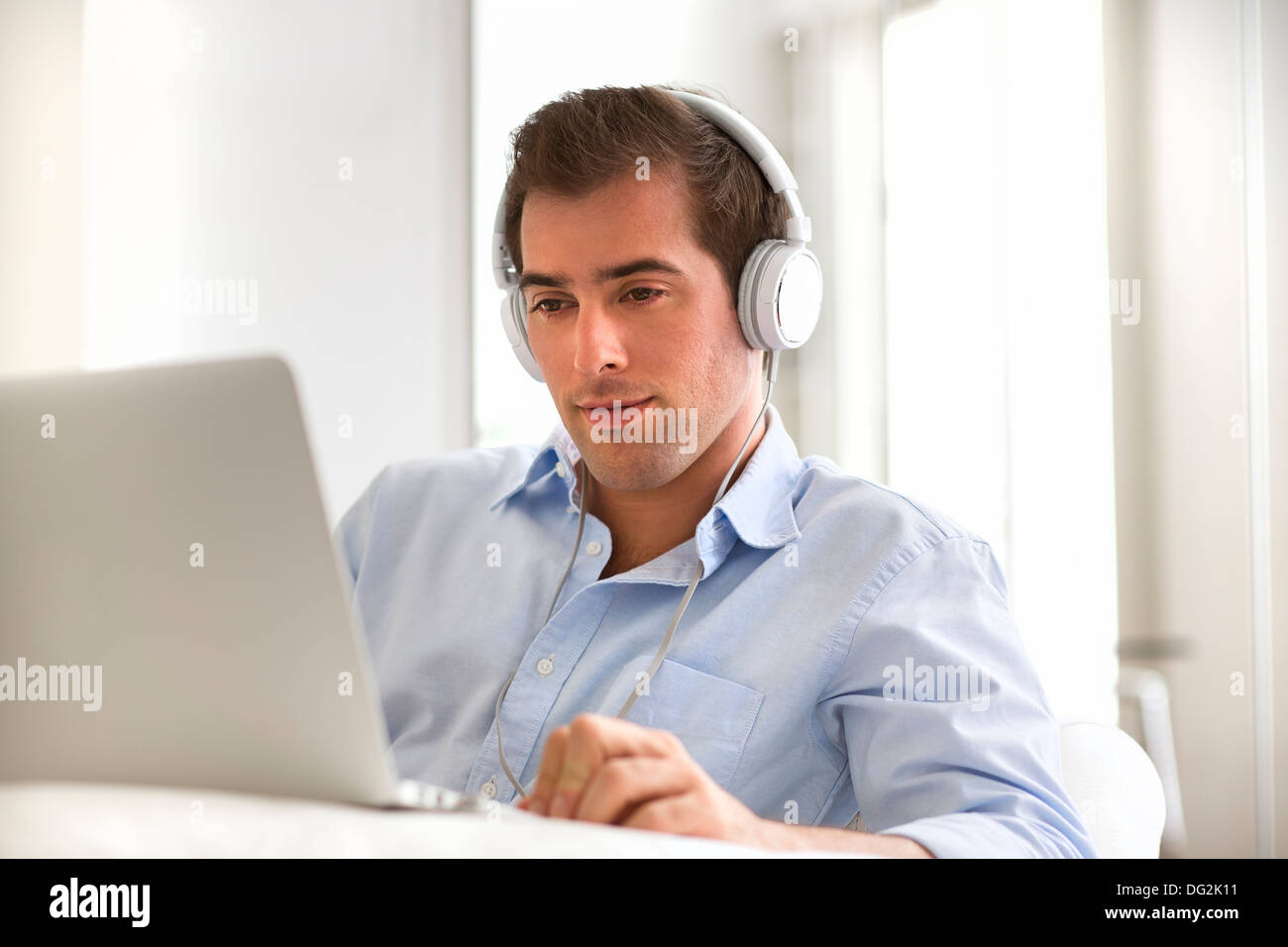 Uomo che ascolta la musica con gli auricolari sul computer portatile, seduto sul divano Foto Stock