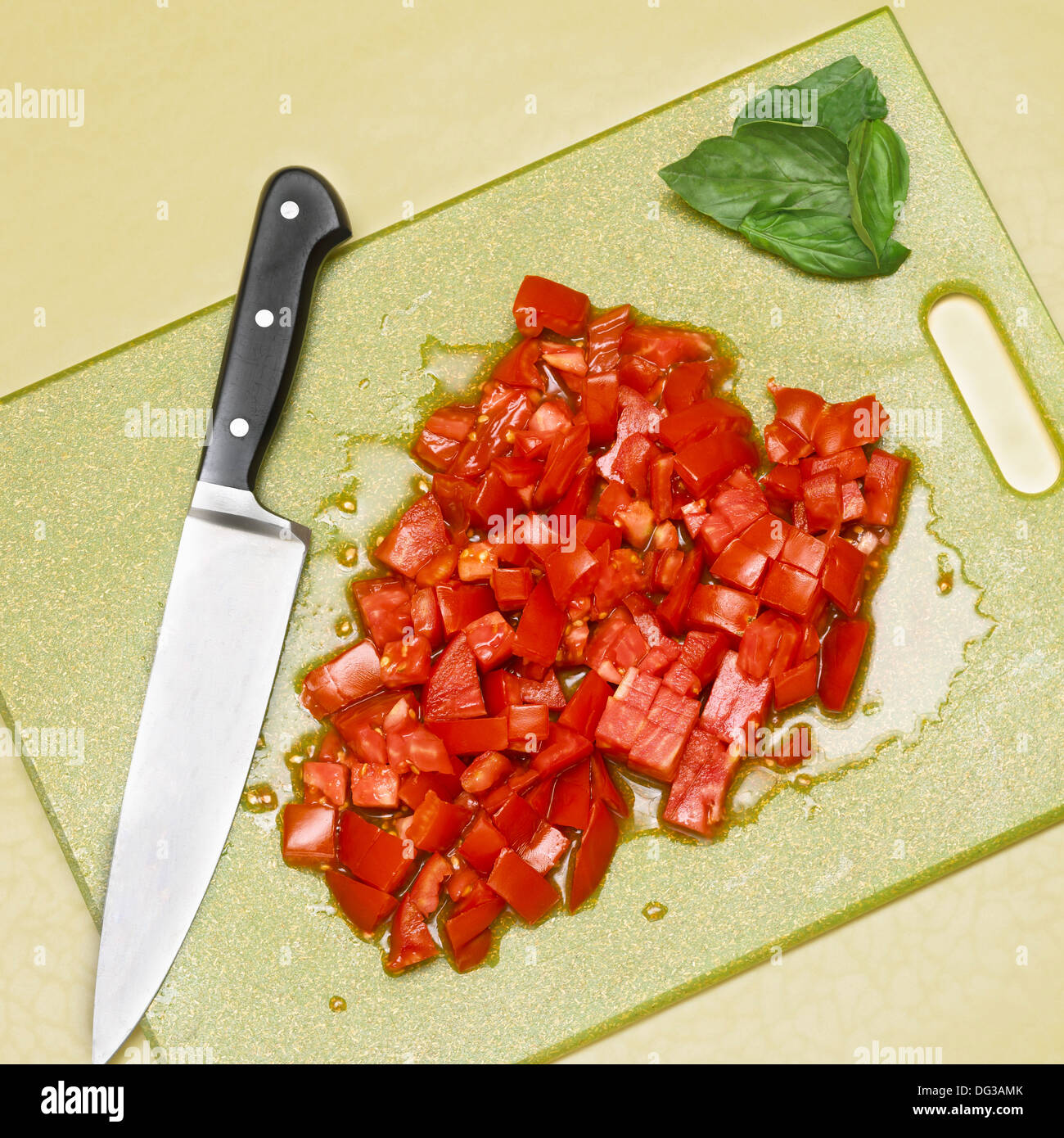Pomodori tagliati a cubetti con basilico e coltello affilato sul tagliere, ad alto angolo di visione Foto Stock