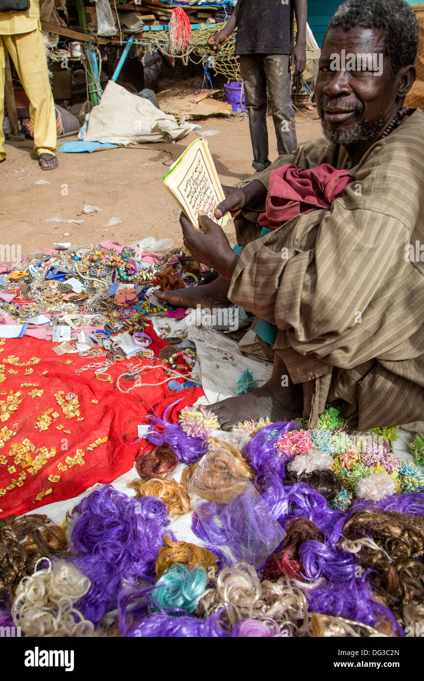 Il Senegal, Touba. Venditore ambulante di orecchini e bigiotteria la lettura di un opuscolo in lingua araba. Foto Stock